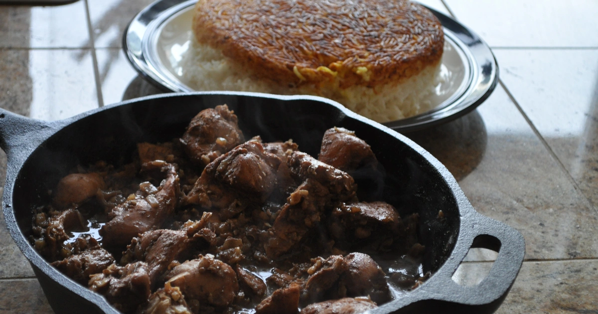 Rich mahogany fesenjan stew with tender chicken in pomegranate walnut sauce garnished with fresh pomegranate arils served over saffron rice at Carnys Restaurant Encino